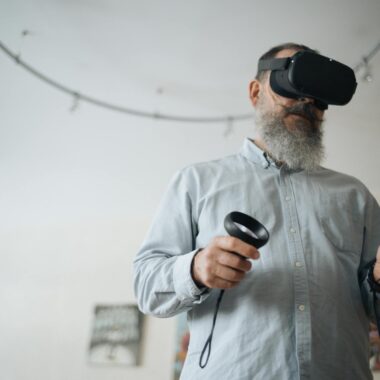 A senior man explores virtual reality using a headset and controllers indoors, showcasing technology interaction.