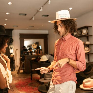 A young interracial couple enjoys trying on fashionable hats at a boutique shop.