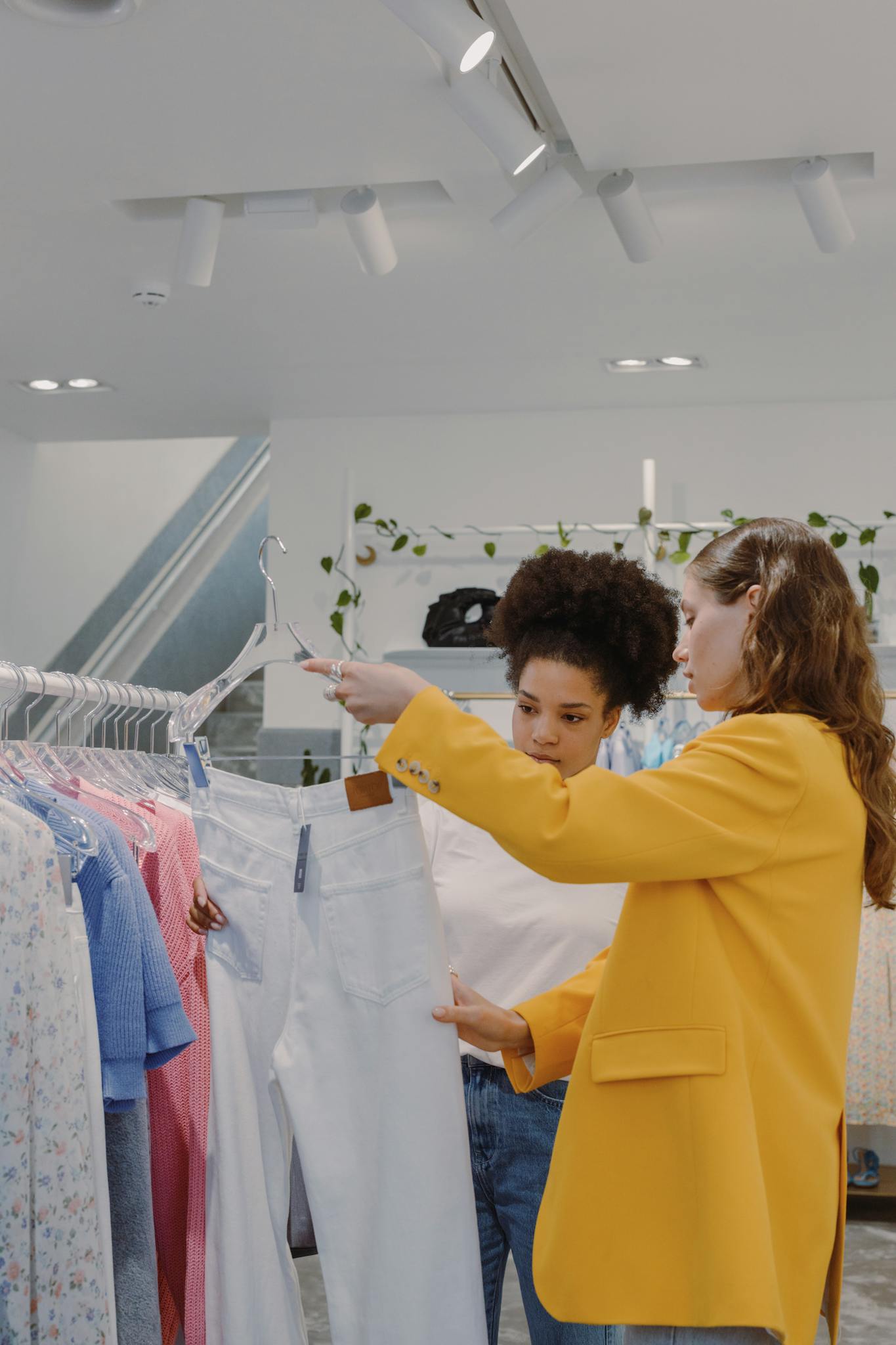 Two women browsing clothes in a stylish boutique, examining white pants.